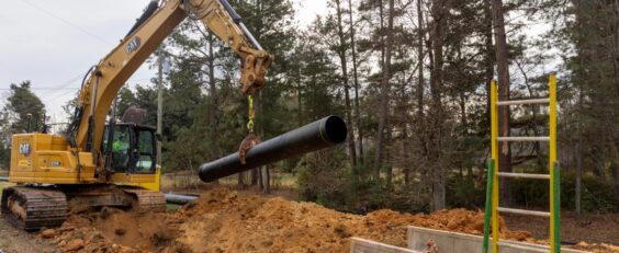 Excavator installing pipe into trench box