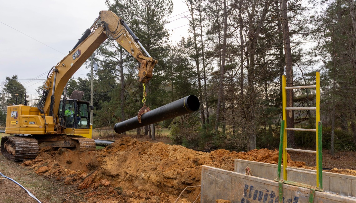 Excavator installing pipe into trench box