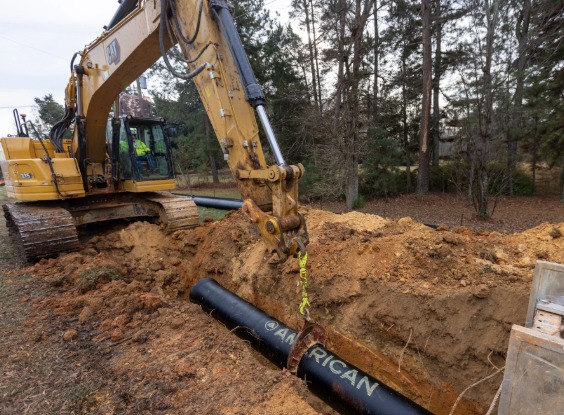 Excavator lowering pipe into ground