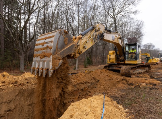 Excavator dumping dirt into trench